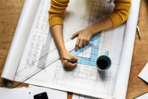 Overhead view of an architect drawing on architectural blueprints with a ruler and triangle.