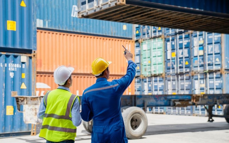 Two workers in hard hats stand beside a shipping container, illustrating the implications of IC-DISC on taxing exports.