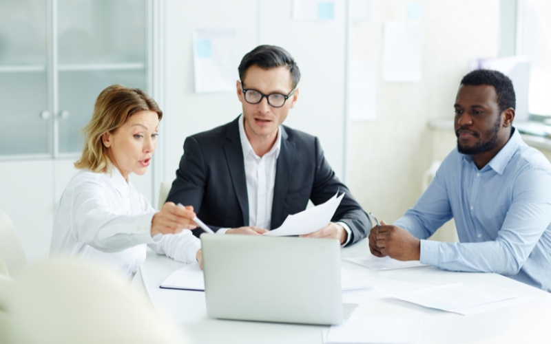 Three business people at a table with a laptop, actively discussing IC-DISC and its comparison to other export tax incentives.