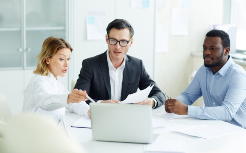 Three business professionals discussing at a table with a laptop, focused on the DISC Tax Structure and Operational Structure.
