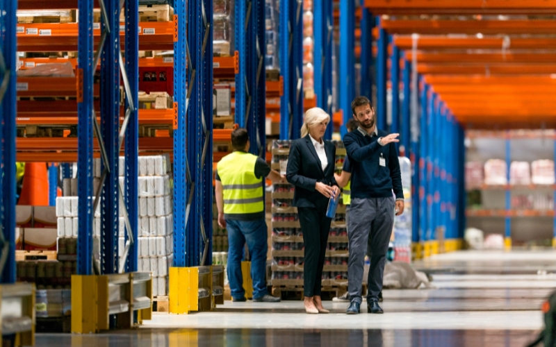 Two people navigating a warehouse with pallets, illustrating the context of IC-DISC FAQs on recordkeeping.
