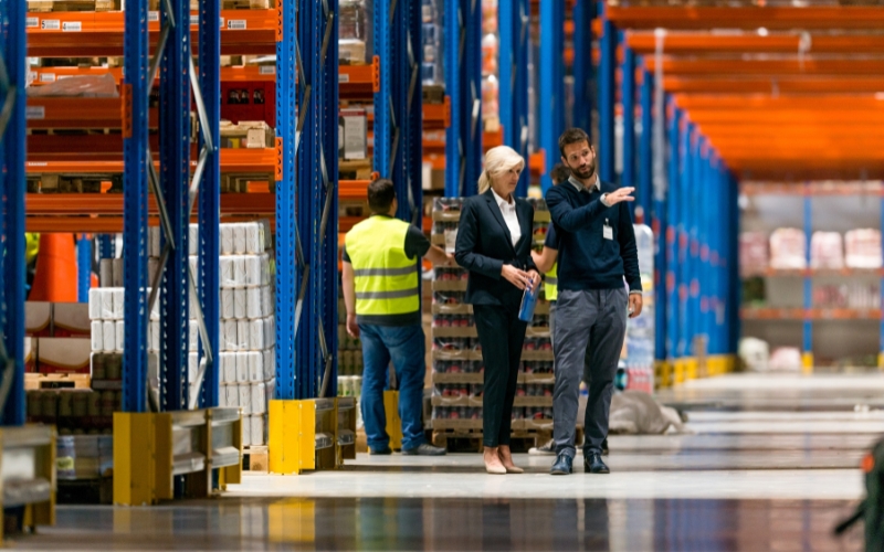 A pair of people navigating a warehouse filled with shelves, exemplifying efficient space use from the 1120-IC-DISC Schedule K.