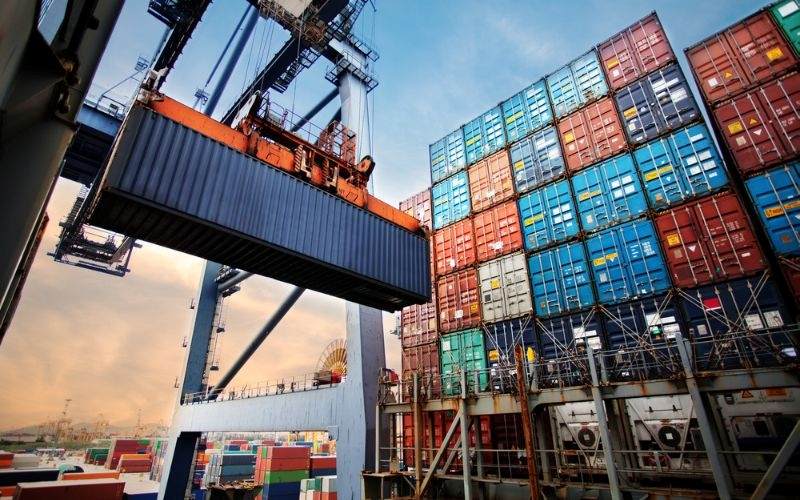 A crane lifts shipping containers at a busy container terminal, illustrating logistics and cargo management operations.