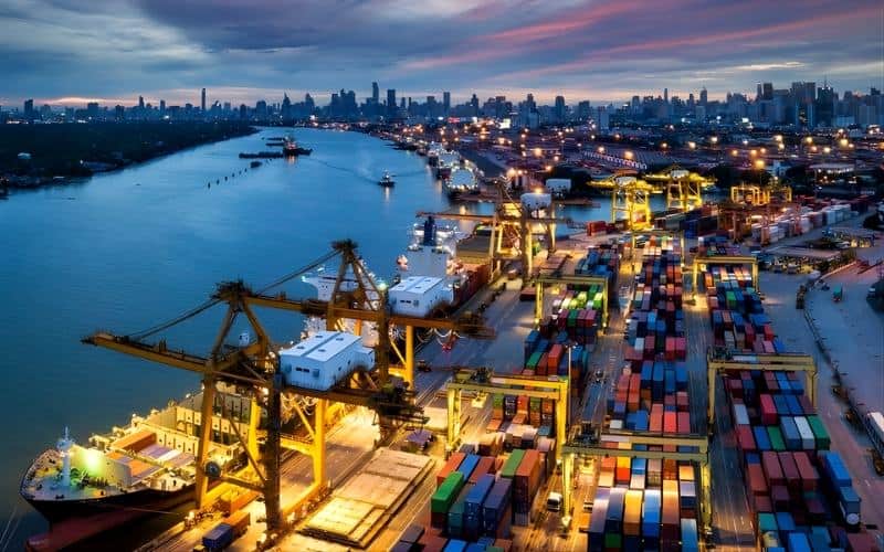 A serene dusk scene of a port filled with cargo containers, reflecting the dynamics of international shipping.