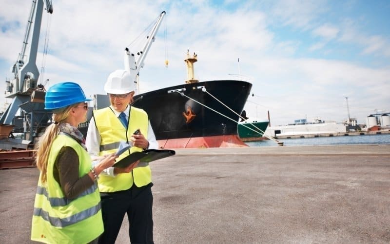 Two people wearing hard hats are positioned in front of a ship, focusing on IC-DISC Commission Payment Rules and compliance.