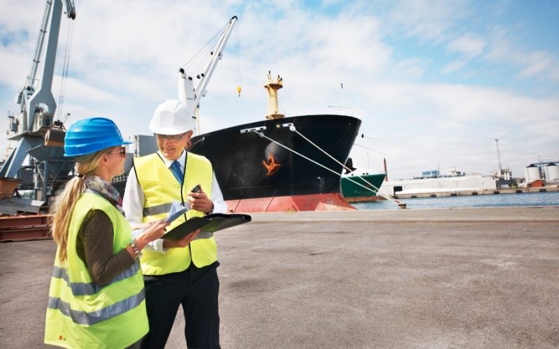 Two people wearing hard hats are positioned in front of a ship, focusing on IC-DISC S-Corp eligibility criteria.