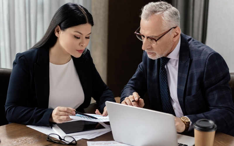 Two professionals in business attire work together on a laptop, discussing IC-DISC and FDDEI calculation methods.