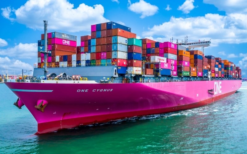 A vibrant pink cargo ship filled with various containers, illustrating the scale of maritime transport and logistics.