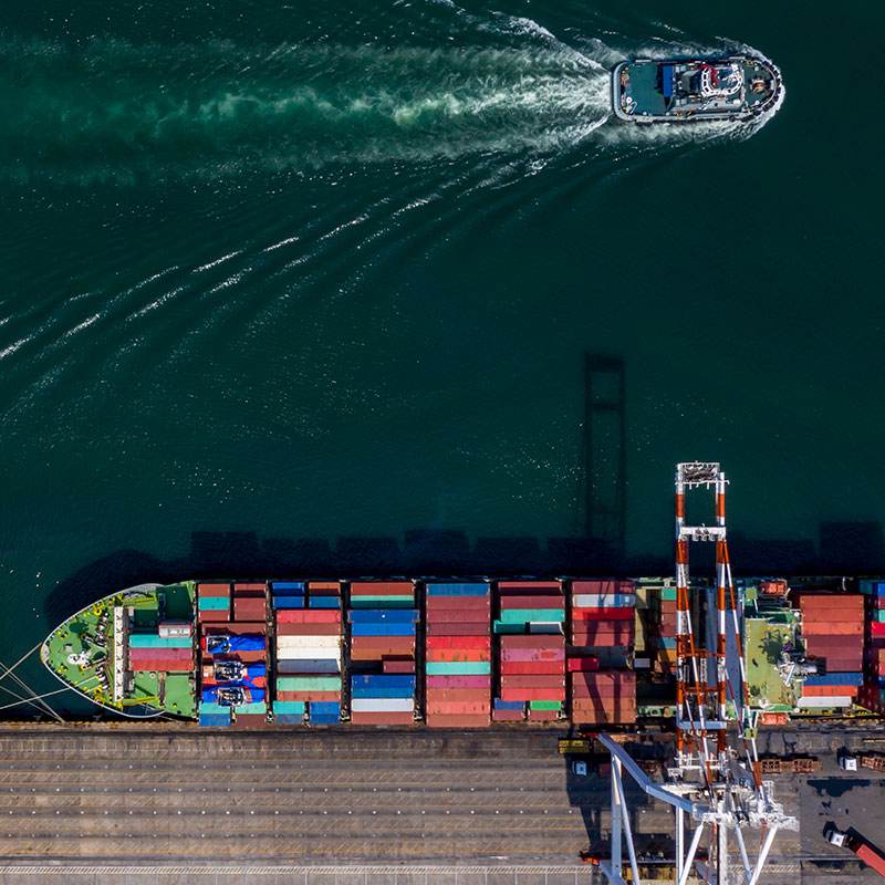 Aerial view of a container ship at a dock and a tugboat moving through the water nearby.