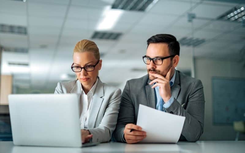 Two colleagues examining a document on a laptop, focused on IC-DISC FAQs and compliance requirements.