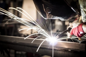 A welder in a protective mask and gloves welding metal, with bright sparks flying.