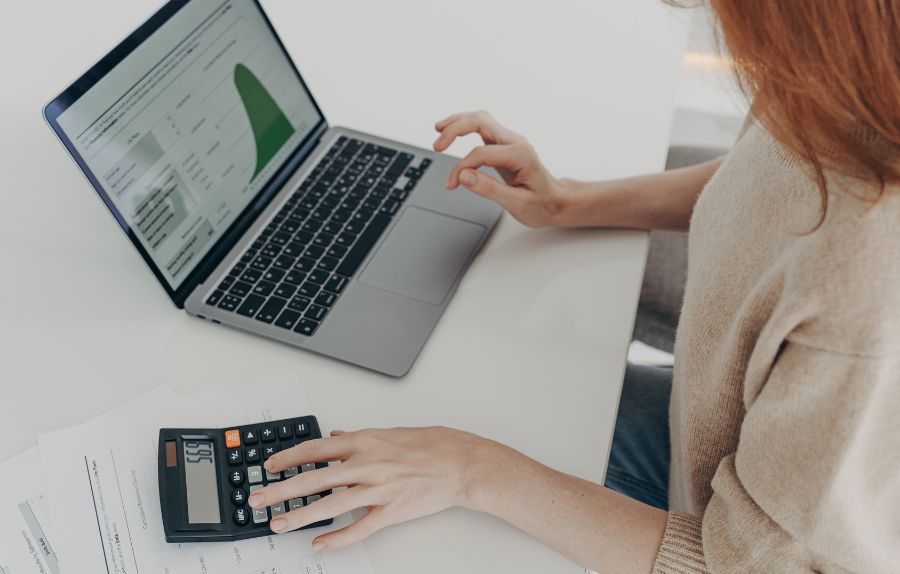 A person using a laptop with data charts and a calculator to perform financial analysis.