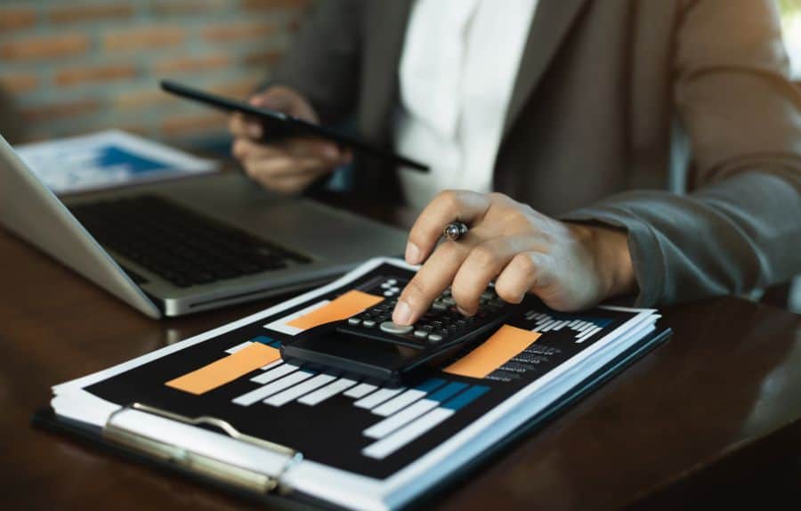 A professional using a calculator on top of financial charts while holding a tablet.